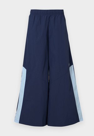 Calças largas de marinha com cintura elástica, apresentando painéis laterais em azul claro e uma textura suave. Projetadas para conforto e facilidade de movimento.