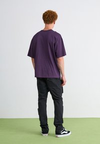 Purple cotton t-shirt, loose fit, paired with black cargo pants. Black and white sneakers complete the outfit. Simple, casual design.