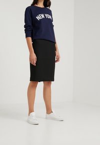 Felpa blu navy con la scritta "NEW YORK" in bianco, abbinata a una gonna a matita nera e sneakers bianche. L'outfit presenta un look casual.
