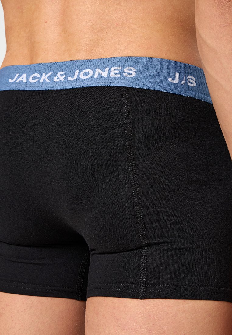Hombre que lleva calzoncillos negros con una cinturilla azul que presenta el logotipo blanco "JACK & JONES".