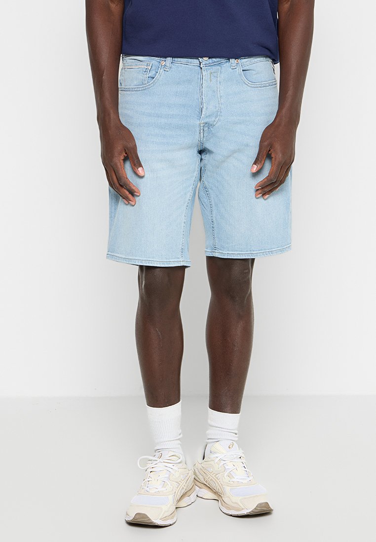 Lichtblauwe denim shorts met een rechte snit, vijf-zakkenontwerp en zichtbare stiksels, gecombineerd met witte sneakers en sokken.