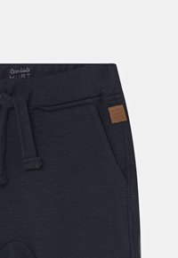 Navyblaue Jogginghosen aus weichem Stoff, mit einem Kordelzugbund, seitlichen Taschen und einem kleinen braunen Leder-Logo-Patch.