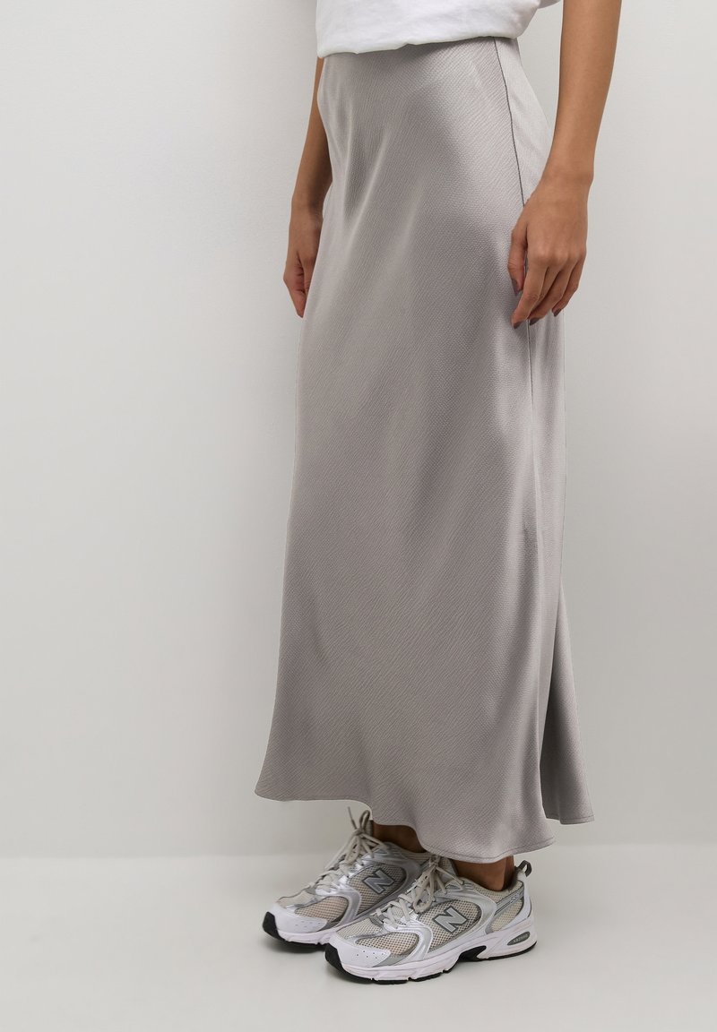 Jupe maxi en satin gris avec une texture subtile et une fente latérale, associée à des baskets athlétiques grises et blanches.