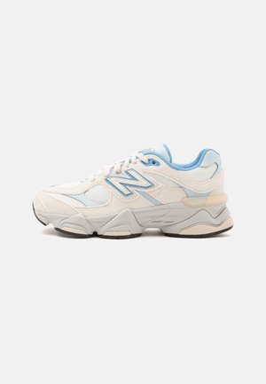 Λευκό και ανοιχτό μπλε sneaker New Balance με επάνω μέρος από δίχτυ και σουέντ, παχιά σόλα και κορδόνια, απεικονίζεται από το πλάι σε απλό φόντο.