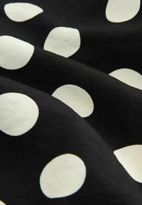 Tissu noir à gros pois blancs, montré en gros plan avec des plis et une texture visibles.