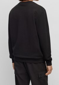 Sudadera negra con cuello redondo, mangas largas y puños acanalados. La tela tiene una textura suave y un corte relajado.