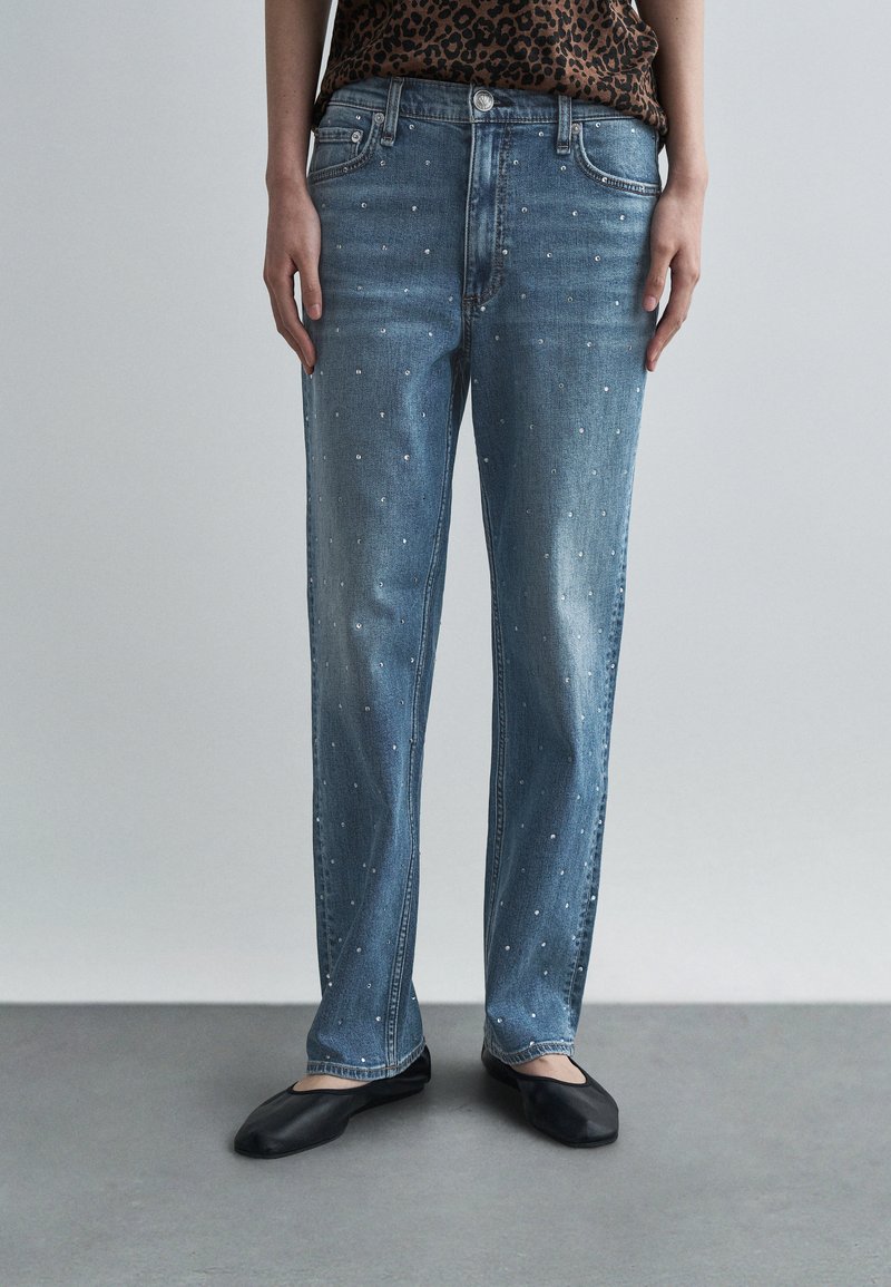 Jasnoniebieskie jeansy o prostych nogawkach z rozsianymi cyrkoniami, pięcioma kieszeniami i wyblakłym praniem. Zestawione z czarnymi płaskimi butami.