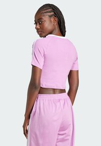 Pink cropped sporty top with short sleeves, white accents on shoulders, paired with matching pink joggers. Smooth fabric and relaxed fit.
