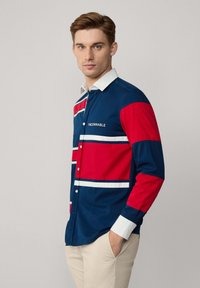 Camisa de botones azul y roja con rayas blancas, con cuello y puños en contraste blanco. Logo "FACONNABLE" en el pecho.