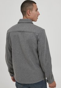 Grå ullblandingsjakke med en skarp krage, knappedeler og en strukturert finish, båret over denimjeans.