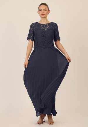 Navy blue dress with a lace bodice and short sleeves, featuring a pleated skirt that flows elegantly, complemented by silver heels.