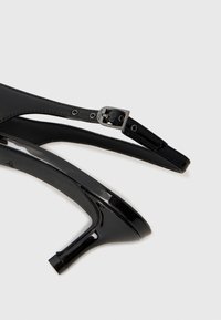 Black patent leather high-heeled shoe with a slender heel, an open toe, and an adjustable ankle strap featuring a metal buckle accent.