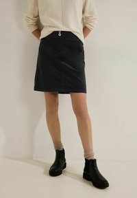 Mørk denimnederdel med lige snit, der har knaplukning foran og sidelommer. Bæres med sorte ankelstøvler og beige sokker.