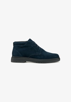 Botas chukka de ante azul marino con punta redonda, diseño con cordones y suela de goma negra con un patrón de textura.