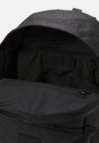 Interno dello zaino nero con rivestimento in tessuto liscio, scomparti e una tasca con zip. Motivo a logo impresso sulla parte esterna.