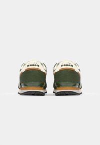 Green and cream sneakers with a suede upper, featuring a brown leather accent and black rubber sole. Branding on the heel is visible.