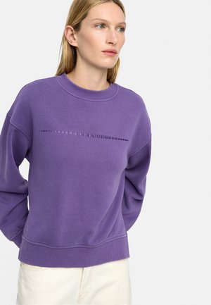 Fioletowa bluza z okrągłym wzorem na klatce piersiowej, z klasycznym okrągłym dekoltem i ściągaczami przy mankietach. Miękki materiał z mieszanki bawełny.