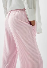 Lightweight, pink striped pants with an elastic waistband and pockets, featuring a soft texture and wide leg cut.
