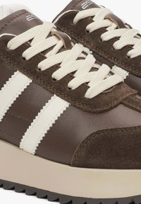 Brązowe skórzane i zamszowe sneakersy z kremowymi paskami, teksturowanymi sznurówkami oraz grubą podeszwą z zygzakowatym wzorem na spodzie.