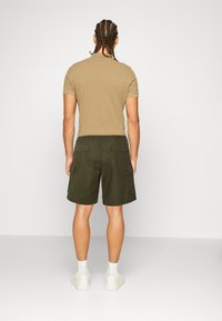 T-shirt beige ajusté et short cargo vert foncé avec poches latérales, portés avec des baskets blanches et des chaussettes, vus de dos.