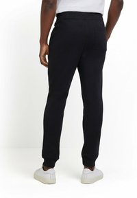 Zwarte joggingbroek met een rekbare tailleband, geribbelde manchetten, achterzakdetails en een gladde stoftextuur, gecombineerd met witte sneakers.