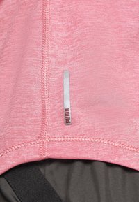 Różowy materiał o melanzowanej fakturze, z srebrną metką logo. Szycie jest widoczne, podkreślając konstrukcję i design odzieży.