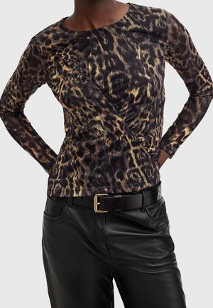 Personne portant un haut à manches longues imprimé léopard rentré dans un pantalon en cuir noir avec une ceinture noire et une boucle dorée, les mains sur les hanches.
