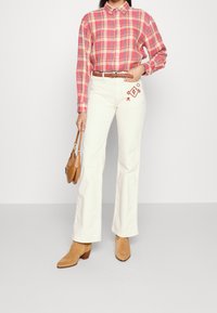 Pruhovaná košile v růžové, žluté a bílé barvě s límečkem. Bílé kalhoty s vyšívaným vzorem. Světle hnědé boty na podpatku a světle béžová kabelka.