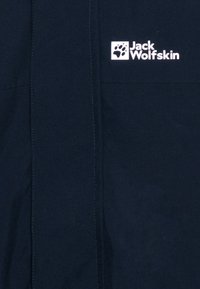 Cămașă bleumarin dintr-un material moale, cu o cusătură verticală și un logo alb, "Jack Wolfskin," însoțit de o amprentă de lăbuță.