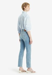 Jeans de color azul claro con un diseño ajustado, que cuentan con bolsillos traseros y un parche de cuero con la marca. Llevados con una camisa de gran tamaño de color azul claro y tacones blancos.