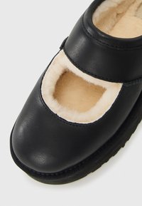 Sorte lædersko med beige fleece-foring og en bred åbning på en hvid baggrund.