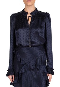 Navy satijnen blouse met een gerimpelde kraag, een sleutelgatstrikdetail en subtiele paisleypatronen. Heeft gathered mouwen en een knoopsluiting aan de voorkant.