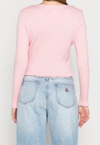 Rosa gerippter Langarmtop mit gewelltem Saum, kombiniert mit hellblauen High-Waist-Jeans mit Gesäßtaschen und einem kleinen Lederlogo-Patch.