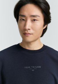 Donkerblauwe sweatshirt van katoen, met een ronde halslijn, geribbelde boorden en een bedrukt logo op de borst in lichtgrijs.