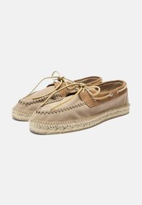 Zapatos de ante beige con detalles de costura, puntera redonda y cierre de cordones. La suela de yute trenzado agrega textura y contraste.