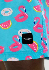 Kék fürdőnadrág rózsaszín flamingó és fánk mintával, az alsó részén egy "JACK & JONES EST.1990" felirattal ellátott címkével.