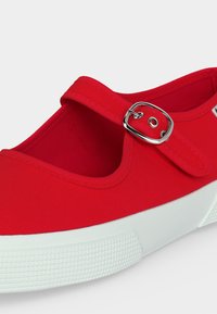 Κόκκινο καμβαδένιο παπούτσι Mary Jane με λευκή λαστιχένια σόλα και ασημί λουράκι με αγκράφα, εμφανίζεται σε κοντινή διαγώνια όψη.