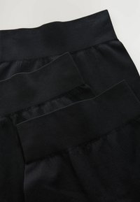 Sorte ribbede leggings stakket, med brede elastiske taljebånd og glat, struktureret stof for komfort og fleksibilitet.