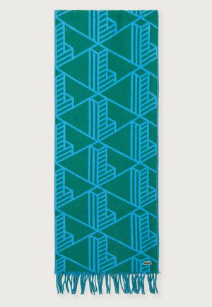 Blauwe sjaal met geometrisch patroon in teal, met driehoeken en strepen, afgewerkt met franjes en een klein logo-label.