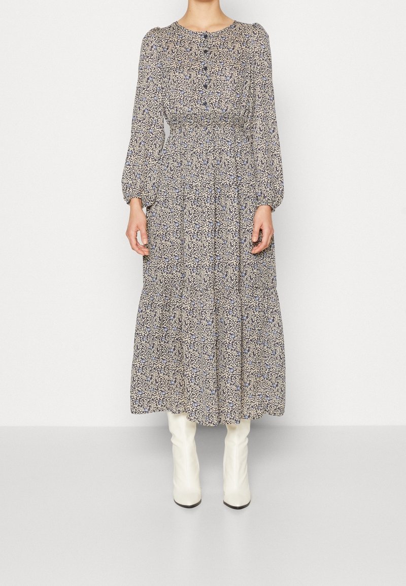 Robe à manches longues, imprimée de fleurs, avec un col rond, des détails de boutons et une taille froncée, associée à des bottes blanches au-dessus du genou.