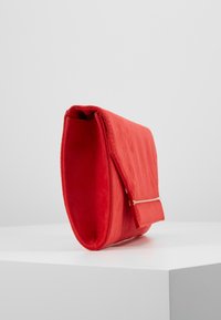 Červené psaníčko z látky s elegantním obdélníkovým tvarem, zdobené zlatým zapínáním a měkkým, texturovaným povrchem.