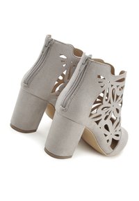 Šedé semišové kotníkové boty mají vyřezávané květinové vzory, otevřenou špičku a masivní podpatek s zipem na zadní straně.