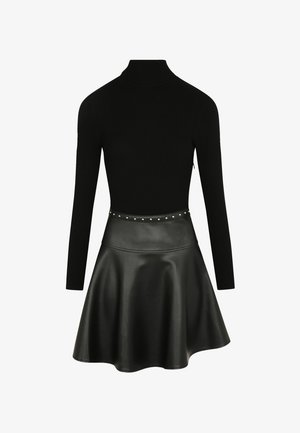 Top negro de canalé con cuello alto combinado con una falda skater de cuero negro que presenta una cinturilla con tachuelas y una textura suave y brillante.