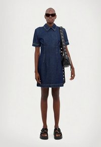 Džinsa kleita ar apkakles izgriezumu, īsām piedurknēm un strukturētu siluetu. Raksturo kontrastējošas šuves, kombinēta ar melniem aksesuāriem.