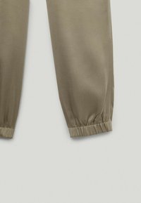 Lyse olivengrønne joggerbukser med elastisk talje og cuffs, der har en glat, let skinnende stoftekstur.