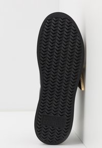 Semelle de chaussure en caoutchouc noir avec motif en chevrons. Présente un logo embossé dans un encadré rectangulaire, avec un accent légèrement surélevé au talon.