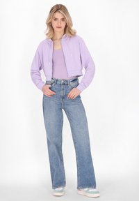 Felpa viola in versione corta con zip frontale, abbinata a jeans a vita alta azzurri e a gamba larga e scarpe da ginnastica multicolore.