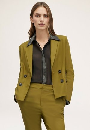Blazer sur mesure vert olive avec un design croisé, boutons noirs et une chemise noire contrastante avec un col orné de sequins.