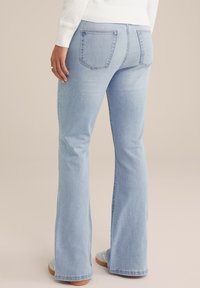 Svijetloplave traperice s proširenim nogavicama izrađene od denima s glatkom teksturom, s dva stražnja džepa i dovršenim rubovima, nosene s sivim tenisicama.