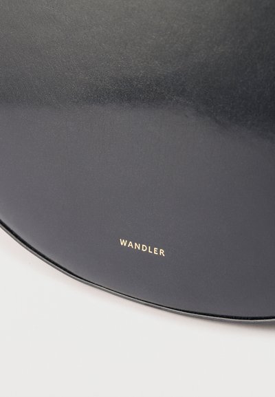 Κοντινή λήψη λείας επιφάνειας μαύρου δέρματος με μικρό, χρυσό ανάγλυφο όνομα μάρκας "WANDLER" που βρίσκεται στο κέντρο κοντά στην κάτω άκρη.